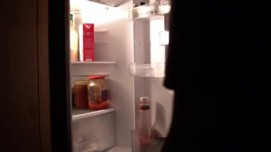 Bir adam gece buzdolabını açar ve bir karton süt alır.