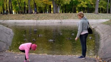 Gölün kenarındaki parkta bir kızla bir kadın ördekleri besliyor.