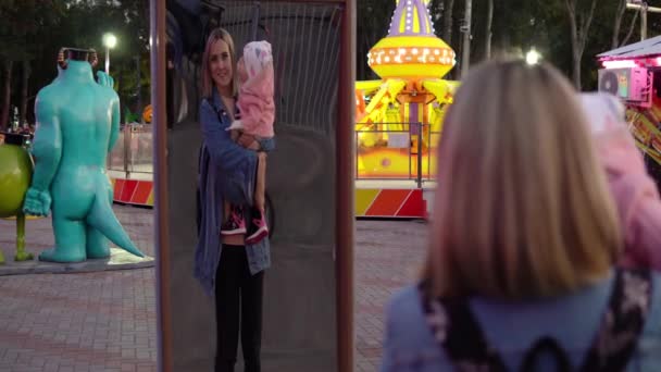 Μια γυναίκα με ένα παιδί στην αγκαλιά της στο πάρκο στέκεται μπροστά από ένα στραβό καθρέφτη — Αρχείο Βίντεο