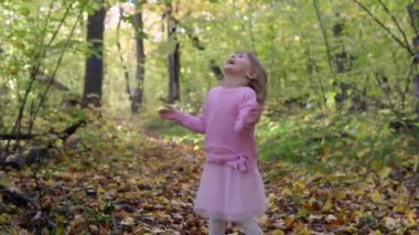 Neşeli bir kız döner ve güz yaprakları üzerine düştüğünde sevinir.