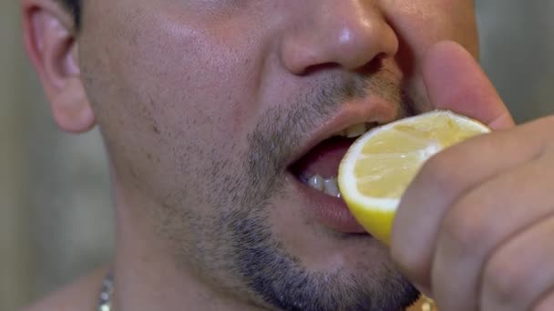 Untidy, unshaven man bites a slice of lemon, and juice flows from his mouth — Stock Video