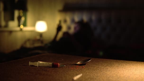 Наркоман лежит на кровати со смартфоном перед применением дозы на заднем плане — стоковое видео