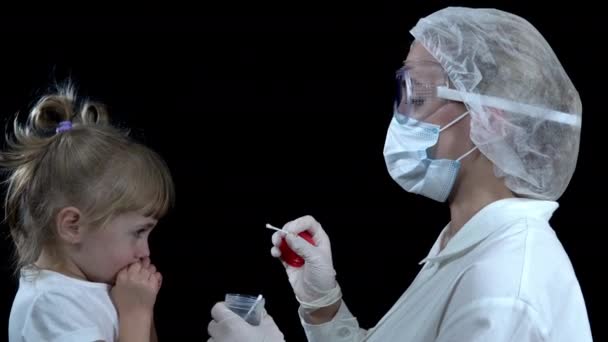 A nurse takes a covid-19 test from a girl. The child takes the analysis on a black background — Stock Video