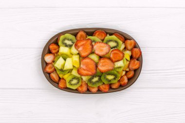 Kivi ananas çilek ve şeftali yaz meyve salatası. Çok lezzetli ve taze görünüyor. Yukarıdan çekilmiş fotoğrafı, tatlı maliyet ahşap beyaz masa üzerinde.