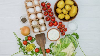 Beyaz ahşap bir masa üzerinde sebze. Yumurta, cerry domates, popatoes, lahana, soğan. 