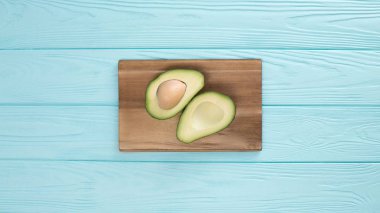 Turkuaz ahşap bir masa üzerinde bir ahşap tahta üzerinde ele geçen avokado.