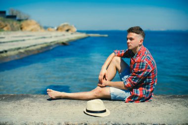 Genç bir adam ekose gömlekli iskelede oturuyordu. O onun şapkasını alıp denizin kenarında uzun zamandır beklenen dinlenme zevk.