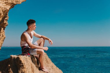 Beyaz gömlekli bir genç adam bir kaya deniz kenarında oturur. O harika bir manzara ve gelecekteki seyahatleri hakkında düşünüyor.