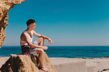 Beyaz gömlekli bir genç adam bir kaya deniz kenarında oturur. O harika bir manzara ve gelecekteki seyahatleri hakkında düşünüyor.