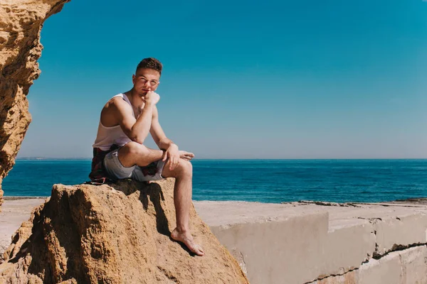 Young Guy Sits Rock Seaside Him Pier Leaned His Arm — Stock Photo, Image