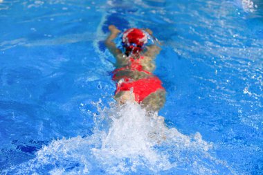 Yüzme havuzunda mavi suyla kırmızı mayo giyen yüzen kadın..