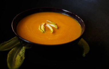 Siyah arka planda salata yapraklı havuç çorbası..