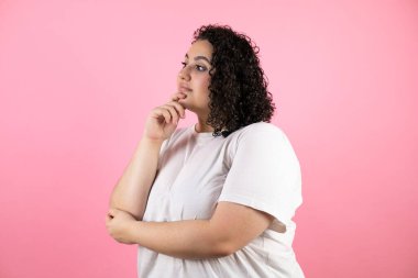 Soyutlanmış pembe arka planda duran genç ve güzel bir kadın. Profilde kendine güveniyor. Kollarını kavuşturup gülümsüyor ve çenesini kaldırıyor.