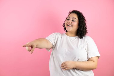 Pembe arka planda genç ve güzel bir kadın sana gülüyor, eli vücudunun üzerinde kamerayı işaret ediyor, utanç ifadesi.