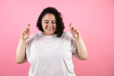 Soyutlanmış pembe arka plan üzerinde genç ve güzel bir kadın umut ve gözlerle gülümseyerek işaret ediyor.