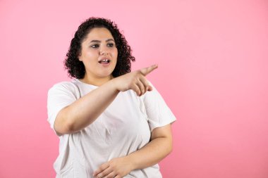 Pembe arka plan üzerinde genç ve güzel bir kadın parmağı önde, ağzı açık, şaşırmış bir ifade, önde bir şey.