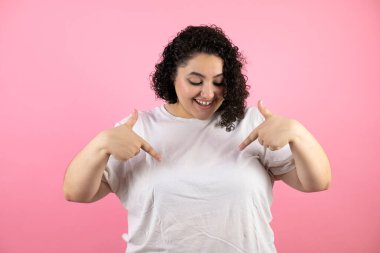 Pembe arka planda genç bir kadın. Günlük giysiler giyiyor. Kendine güvenen, gülümseyen, kendini gururlu ve mutlu gösteren biri..