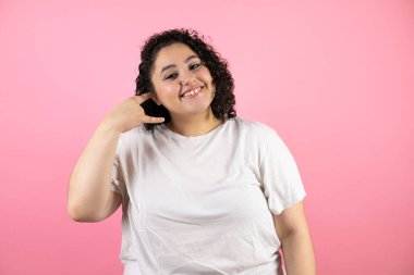 Soyutlanmış pembe arka planda güzel bir kadın gülümsüyor telefonla el ve parmaklarıyla jest yapıyor telefonda konuşuyor gibi.