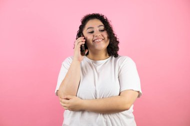 Genç ve güzel bir kadın telefonda konuşuyor, pembe arka planda gülümsüyor..