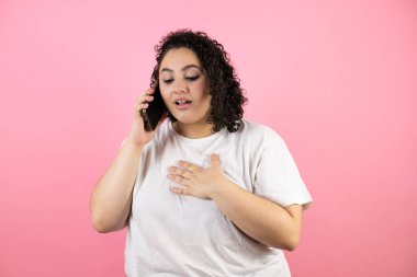 Pembe arka planda endişeli bir ifadeyle telefonda konuşan genç ve güzel bir kadın..