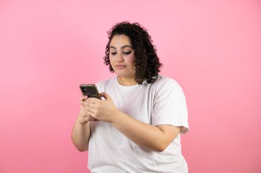 Genç ve güzel bir kadın telefonuyla mesaj atıyor. Pembe arka planda gülümsüyor..