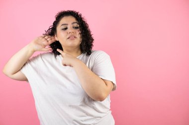 Genç ve güzel bir kadın pembe arka planda dikiliyor. Kulağı kulağında gülümsüyor. Dedikoduları ve dedikoduları dinliyor.