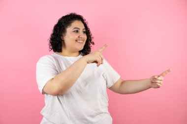 Soyutlanmış pembe arka planda güzel bir kadın gülümsüyor, parmakları ve kolları havada.