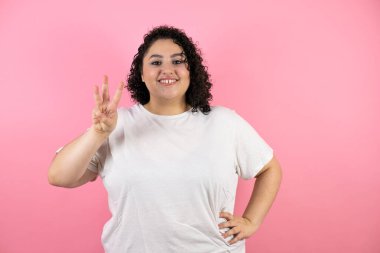 Güzel genç bir kadın kendini beğenmiş ve mutlu bir şekilde gülümserken üç numarayı gösterip işaret ediyor.