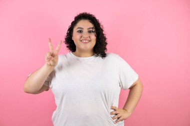 Güzel genç bir kadın kendini beğenmiş ve mutlu bir şekilde gülümserken iki numarayı gösterip işaret ediyor.