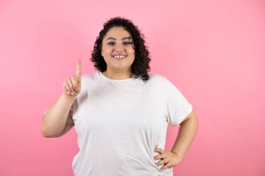 Güzel genç bir kadın bir numaralı parmaklarıyla gösterip işaret ederken kendinden emin ve mutlu bir şekilde gülümsüyor.