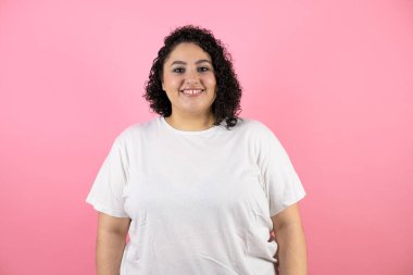 Genç, güzel bir kadın pembe arka planda durmuş gülümsüyor.