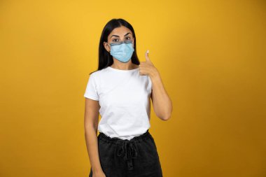 Coronavirus maskesi takan genç ve güzel bir kadın. İzole edilmiş sarı bir arka planda dikiliyorum. Covid19