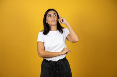 Güzel bir kadının fikri var. İzole edilmiş sarı bir arkaplanda duran günlük beyaz bir tişört giyiyor.