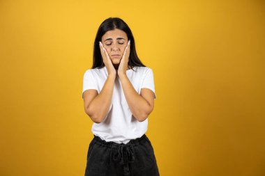 Güzel bir kadın mavi arka planda dikiliyor. Baş ağrısı, çaresiz ve stresli. Çünkü elleri başının üstünde acı ve migren var.