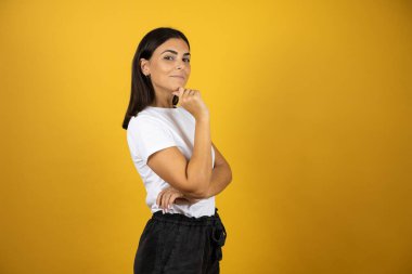 İzole edilmiş sarı arka planda duran güzel bir kadın. Profilde kendine güveniyor. Kollarını kavuşturup gülümsüyor ve çenesini kaldırıyor.