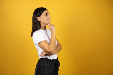 İzole edilmiş sarı arka planda duran güzel bir kadın. Profilde kendine güveniyor. Kollarını kavuşturup gülümsüyor ve çenesini kaldırıyor.