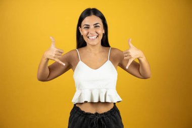 İzole edilmiş mavi arka planda genç ve güzel bir kadın çılgın bir ifadeyle el kaldırarak rock sembolü yapıyor.