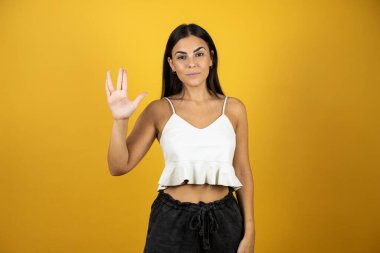 İzole edilmiş sarı arka planda genç ve güzel bir kadın Star Trek ucube sembolü yapıyor.