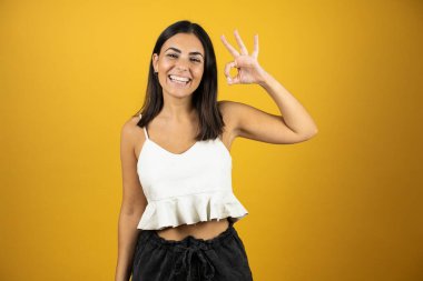 İzole edilmiş sarı arka planda duran genç ve güzel bir kadın. Parmaklarıyla imza atıyor. Mükemmel bir sembol.