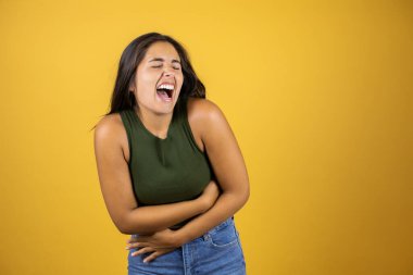 Genç, güzel bir kadın, izole edilmiş sarı arka planda duruyor, gülümsüyor ve kahkahalar atıyor.