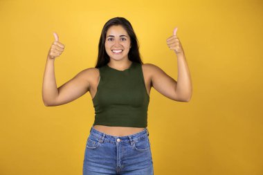 Sarı arka planda duran güzel bir kadın gülümsüyor ve parmaklarıyla işaret veriyor.