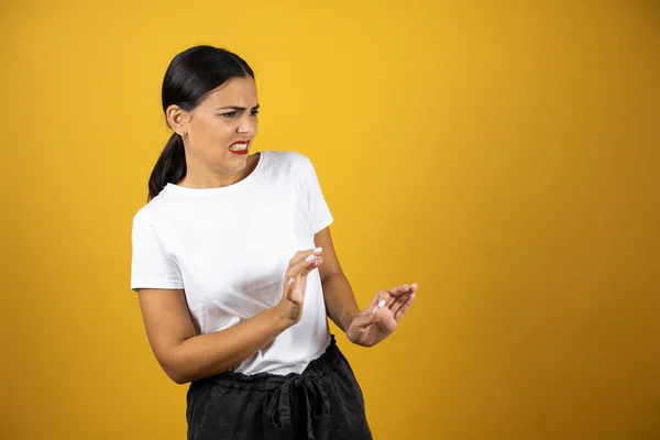 Young beautiful woman with a disgusted expression on her face looking to the right on yellow background. Wearing a white t-shirt and black shorts.