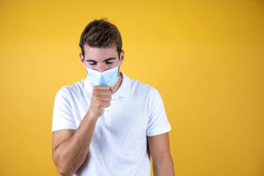 Tecrit edilmiş arka planda maske takan yakışıklı bir adam kendini iyi hissetmiyor ve soğuk algınlığı veya bronşitin belirtisi olarak öksürüyor. Sağlık hizmetleri kavramı.