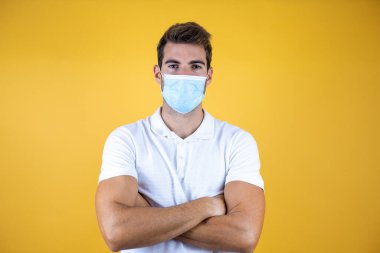 Tıbbi maske takan ve kollarını kavuşturup kameraya gülümseyen genç yakışıklı bir adam. pozitif kişi.
