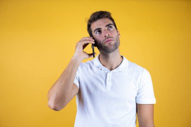 Sarı arka planda akıllı telefon kullanan genç bir adam şaşırmış bir yüzle konuşuyor..