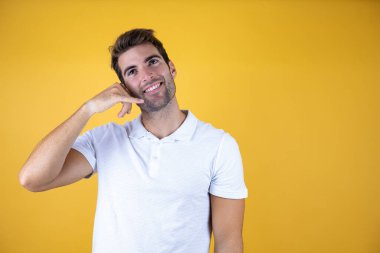 Soyutlanmış sarı arka planda genç yakışıklı adam telefonla el ve parmaklarıyla, telefonla konuşuyor gibi gülümsüyor.