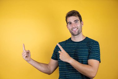 Soyutlanmış arka planda genç yakışıklı bir adam. Gülümsüyor, gülümsüyor ve iki parmağıyla yüzünü gösteriyor.