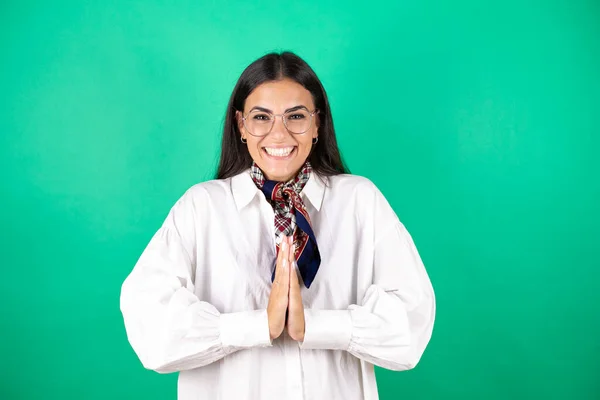 Young beautiful business woman over isolated green background begging and praying with hands together with hope expression on face very emotional and worried