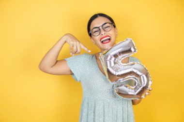 Sarı arka planda duran gözlüklü güzel bir kadın gülümseyerek beş numarayı tutuyor. Aniversary