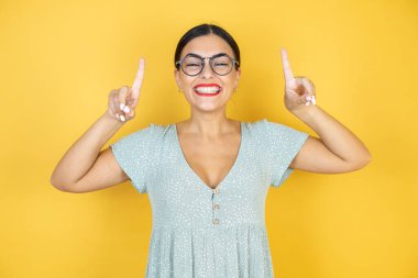 Sarı arka plan üzerine günlük yeşil elbise giyen genç ve güzel bir kadın parmaklarıyla gösterip kollarını kaldırmasına şaşırmış ve şaşırmıştı.